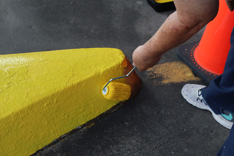 Facilities Maintenance professional refreshing the yellow paint inside a parking garage.